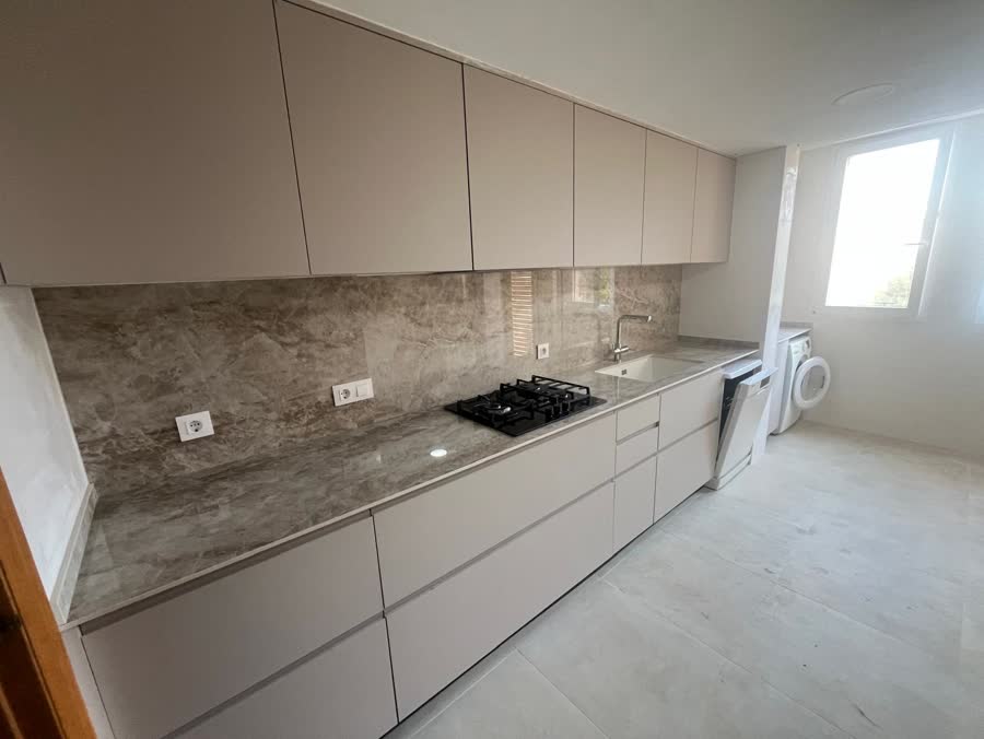 Cocina lineal con muebles color arena y frente de porcelánico efecto piedra
