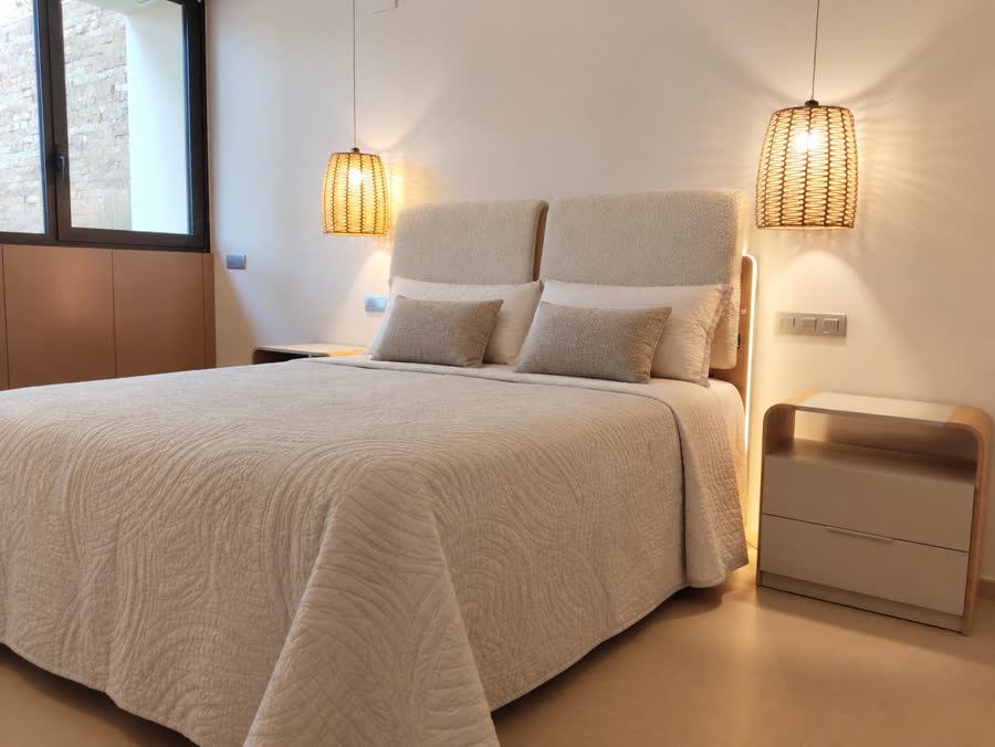 Dormitorio con cabecero tapizado, lámparas de fibra y colcha clara