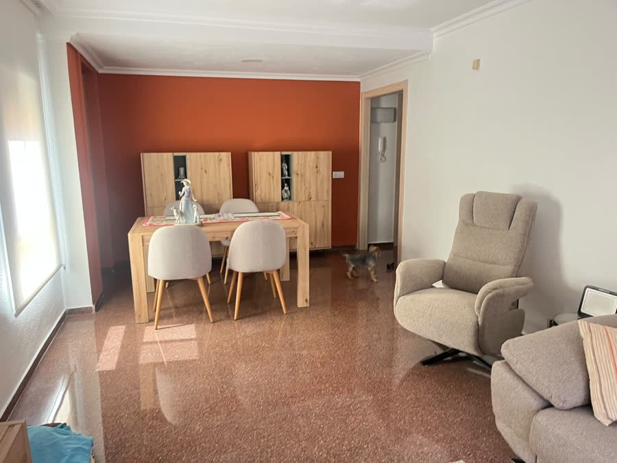 Comedor tras la reforma integral: mesa y aparadores de madera clara sobre pared terracota