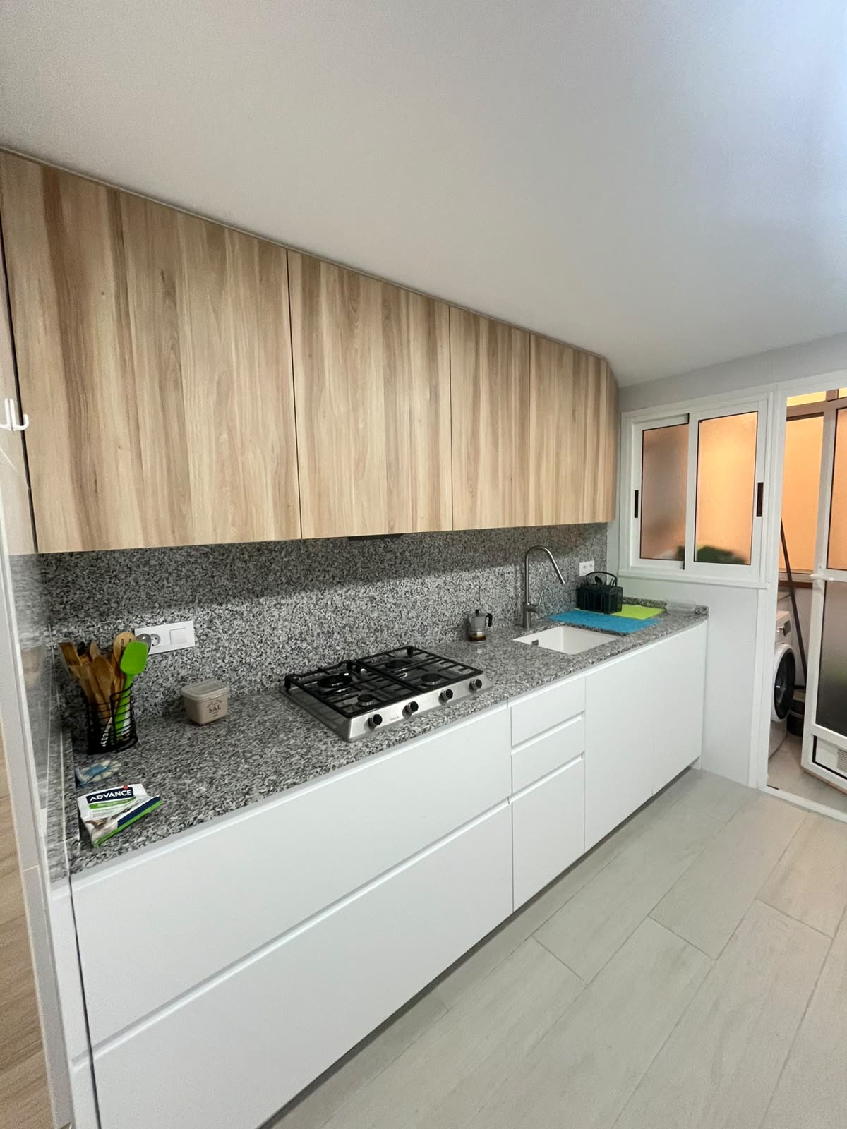 La misma cocina tras la reforma integral — muebles blancos y madera, encimera de granito